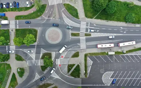Widok z lotu ptaka na rondo i skrzyżowanie. Samochody i autobusy poruszają się po drogach. Zjazd z ronda na który pas?