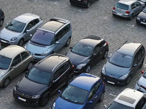 Na parkingu stoi wiele samochodów. Jeden z nich, srebrny Nissan, wygląda na uszkodzony. Czy to szkoda parkingowa? Policja już tu jest.