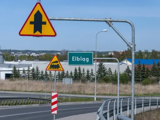 Uwaga na skrzyżowanie z drogą podporządkowaną i przejazd kolejowy. Znak "Elbląg" zaprasza do miasta.