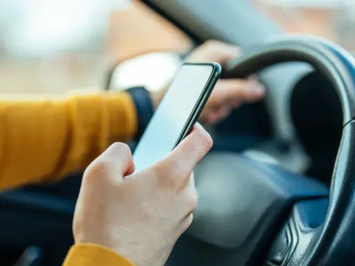 Ręka trzymająca telefon za kierownicą. Zastanawiasz się, ile punktów za telefon stracisz?
