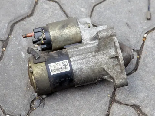 Dwa używane rozruszniki samochodowe, gotowe do wymiany. Jeden z nich ma naklejkę z numerem MC0JT82081.