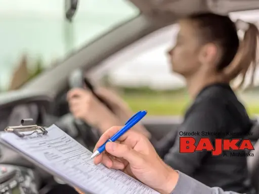 Paraliżujący stres przed egzaminem na prawo jazdy. Egzaminator notuje uwagi, młoda kobieta za kierownicą.