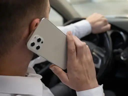 Mężczyzna rozmawia przez telefon, trzymając kierownicę. Ryzykowne korzystanie z telefonu podczas jazdy.
