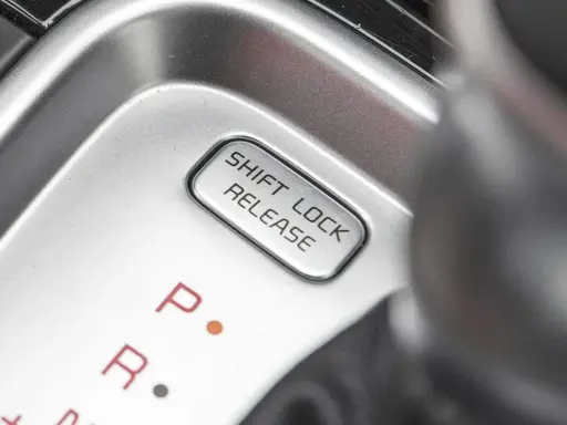 Przycisk "SHIFT LOCK RELEASE" na konsoli środkowej, obok oznaczeń biegów P i R.