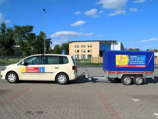 Jasny samochód z przyczepą szkoleniową, na której widnieje napis "KATEGORIE" i logo szkoły jazdy "Expert".