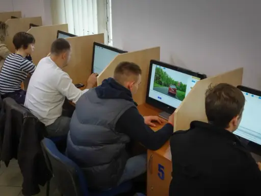 Ludzie siedzą przy komputerach, rozwiązując testy. To miejsce, gdzie można sprawdzić, kiedy można zdawać egzamin teoretyczny na prawo jazdy.