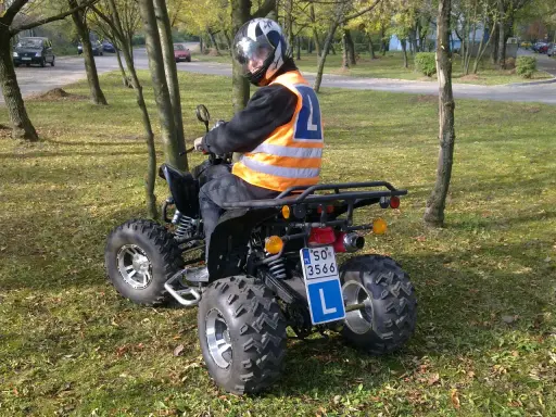Chcesz wiedzieć, jakie prawo jazdy na quada? Kierowca w kamizelce odblaskowej i kasku siedzi na quadzie, gotowy do jazdy.