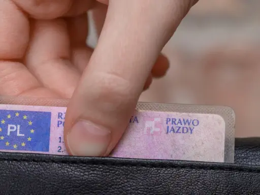 Dłoń wkłada do portfela polskie prawo jazdy. Czy trzeba mieć przy sobie dokument?