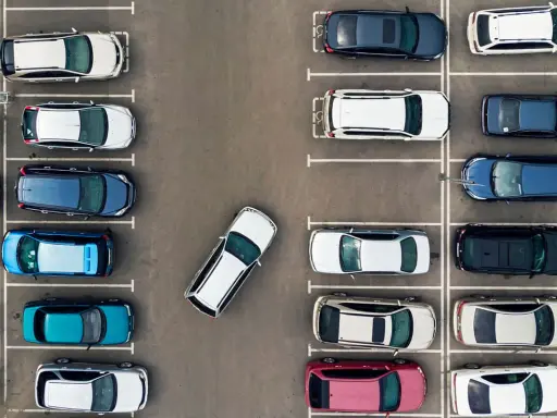 Widok z góry na parking. Po prawej stronie zaparkowane są samochody w rzędzie, jeden za drugim.