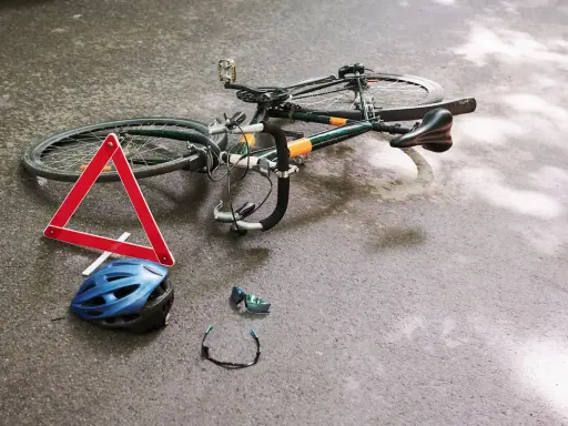 Potrącenie rowerzysty na ścieżce rowerowej. Leżący rower, kask, okulary i trójkąt ostrzegawczy sugerują wypadek.
