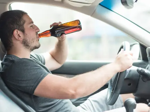 Mężczyzna pije piwo za kierownicą. Powyżej 0,5 promila jaka kara grozi za jazdę pod wpływem alkoholu.