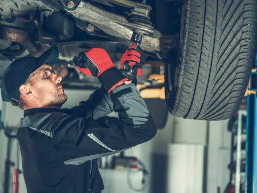 Mechanik dokręca sworzeń w zawieszeniu auta, pracując pod podniesionym pojazdem.