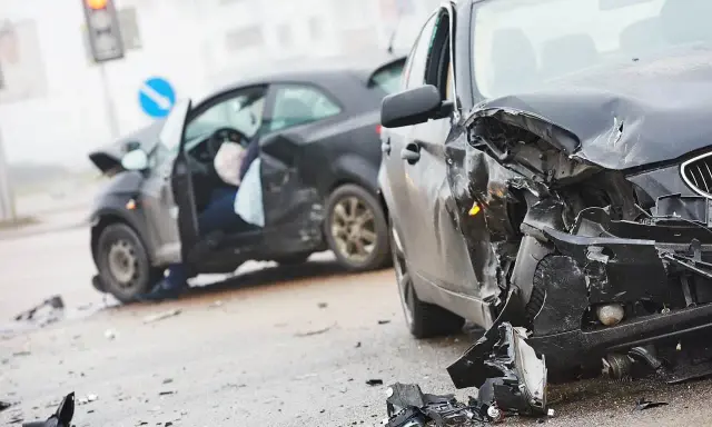 Dwa zniszczone samochody na drodze. W jednym z nich widać siedzącego człowieka po wypadku samochodowym, z otwartymi drzwiami i poduszką powietrzną.