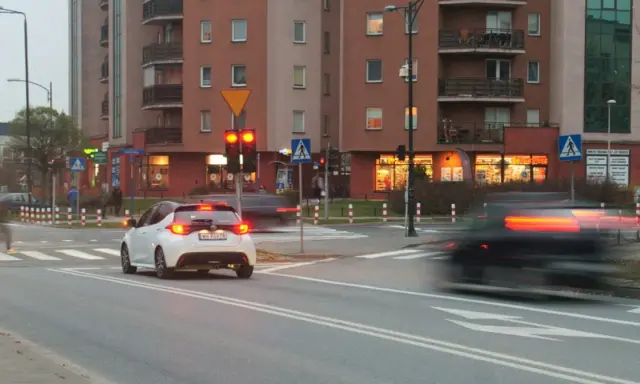 Biały samochód czeka na zielone światło. Czerwone światło oznacza punkty karne.