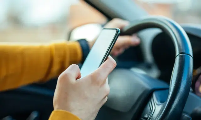 Ręka trzymająca telefon za kierownicą. Zastanawiasz się, ile punktów za telefon stracisz?