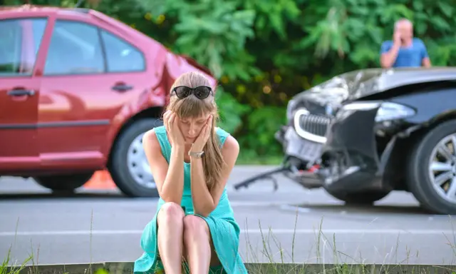 Kobieta w szoku po spowodowaniu wypadku z uszczerbkiem na zdrowiu powyżej 7 dni. Dwa uszkodzone samochody na drodze.