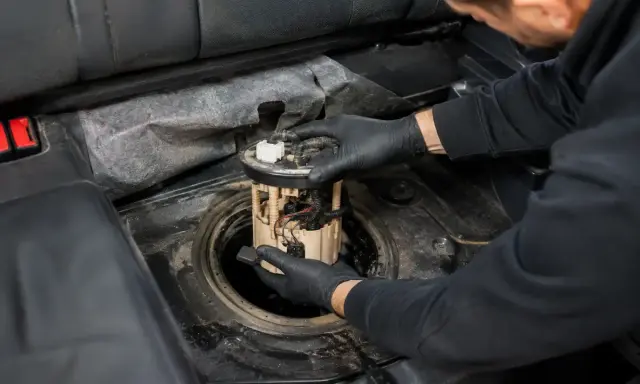 Mechanik w czarnych rękawiczkach wyjmuje moduł pompy paliwa z baku samochodu. To może być objaw uszkodzonej pompy paliwa.