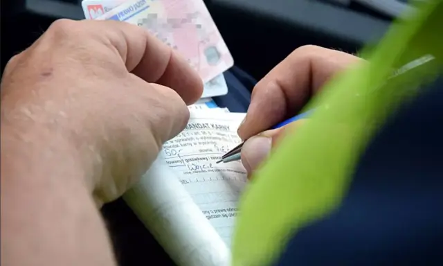 Ręce wypełniają formularz mandatu karnego, próbując dokonać przepisanie mandatu na inną osobę. Widoczne prawo jazdy.