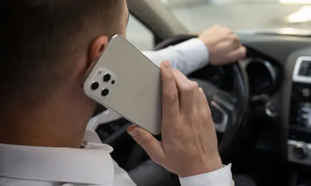 Mężczyzna rozmawia przez telefon, trzymając kierownicę. Ryzykowne korzystanie z telefonu podczas jazdy.