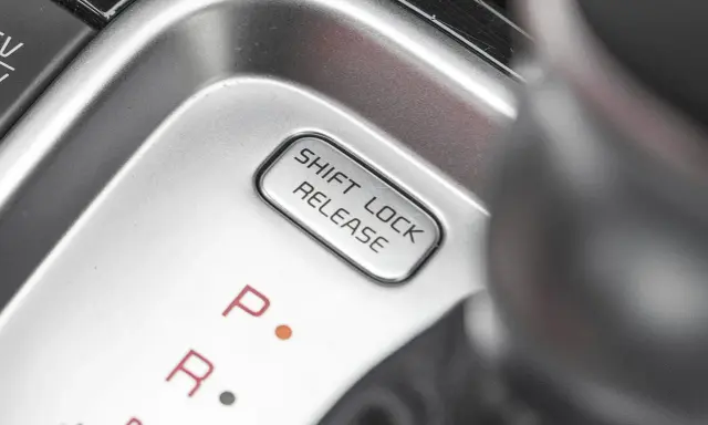 Przycisk "SHIFT LOCK RELEASE" na konsoli środkowej, obok oznaczeń biegów P i R.