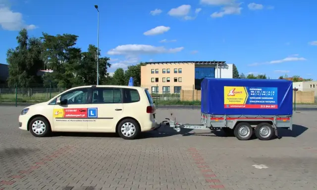 Jasny samochód z przyczepą szkoleniową, na której widnieje napis "KATEGORIE" i logo szkoły jazdy "Expert".