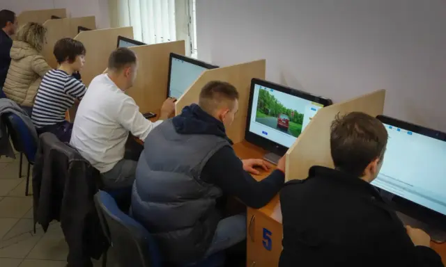 Ludzie siedzą przy komputerach, rozwiązując testy. To miejsce, gdzie można sprawdzić, kiedy można zdawać egzamin teoretyczny na prawo jazdy.