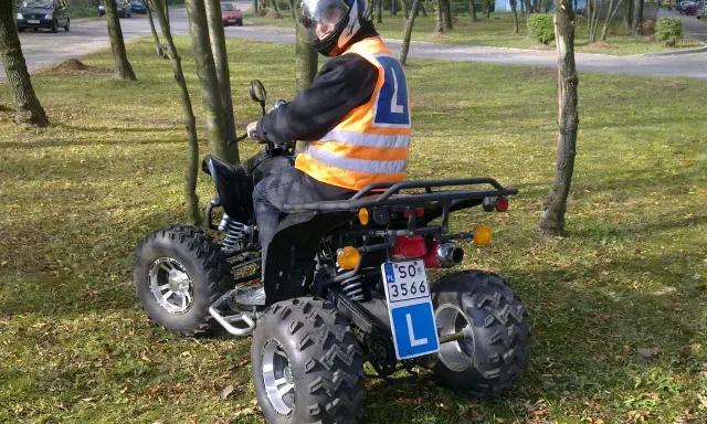 Chcesz wiedzieć, jakie prawo jazdy na quada? Kierowca w kamizelce odblaskowej i kasku siedzi na quadzie, gotowy do jazdy.