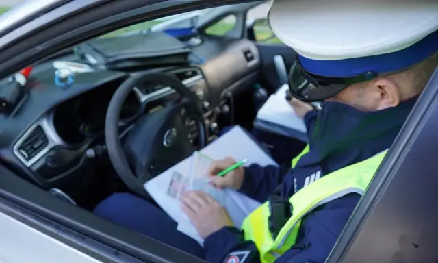 Policjant w radiowozie wypisuje mandat za jazdę bez kasku.
