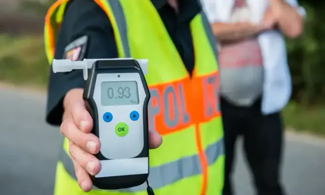 Policjant trzyma alkomat, który pokazuje wynik 0.93. To urządzenie pomaga sprawdzić, co neutralizuje alkohol w wydychanym powietrzu.