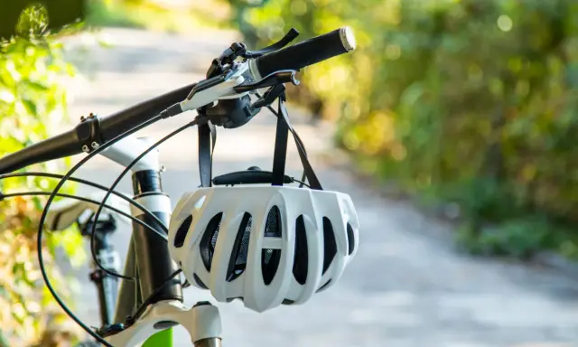 Biały kask rowerowy wisi na kierownicy roweru. Pamiętaj o kasku, by uniknąć mandatu za brak kasku na rowerze.