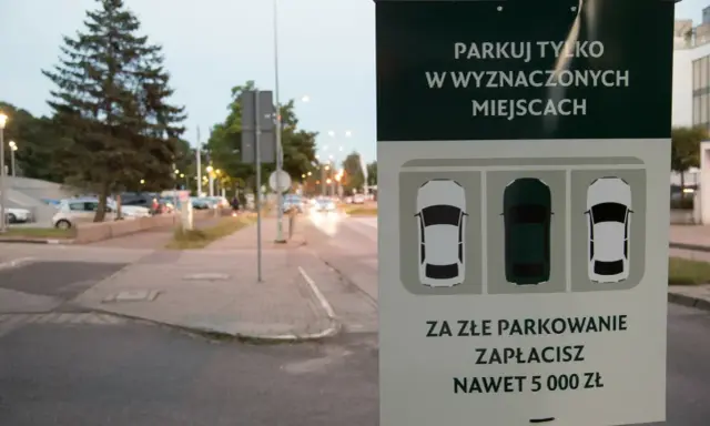 Znak informuje: "Parkuj tylko w wyznaczonych miejscach. Za złe parkowanie zapłacisz nawet 5000 zł". Straż miejska pilnuje porządku.