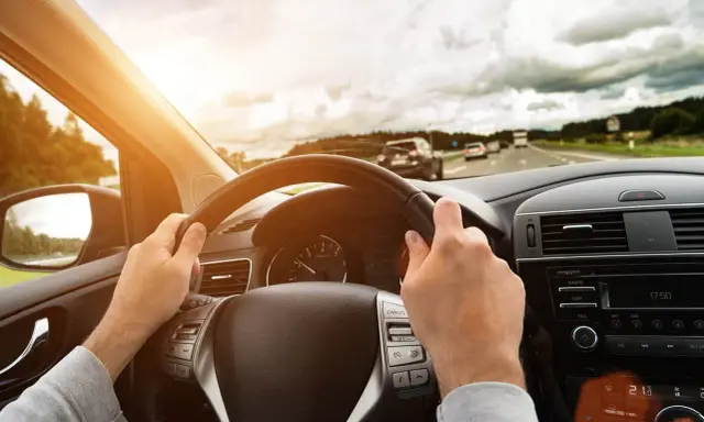Kierowca trzyma kierownicę, jadąc autostradą. Wibracje kierownicy mogą sygnalizować objawy krzywej tarczy hamulcowej.