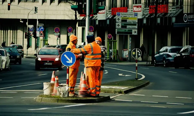 Pracownicy drogowi kierują ruchem, sugerując potencjalne odszkodowanie za brak dojazdu do posesji z powodu robót.