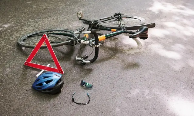 Potrącenie rowerzysty na ścieżce rowerowej. Leżący rower, kask, okulary i trójkąt ostrzegawczy sugerują wypadek.