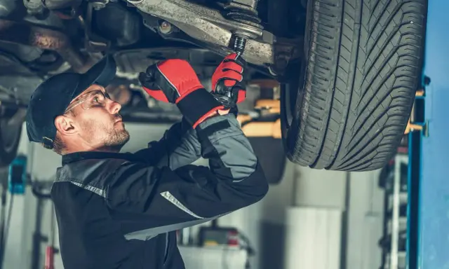 Mechanik dokręca sworzeń w zawieszeniu auta, pracując pod podniesionym pojazdem.