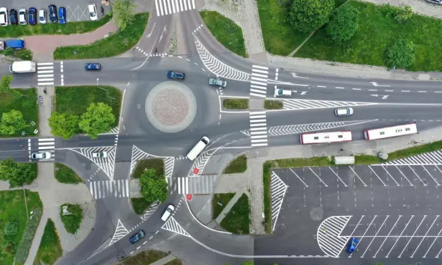 Widok z lotu ptaka na rondo i skrzyżowanie. Samochody i autobusy poruszają się po drogach. Zjazd z ronda na który pas?
