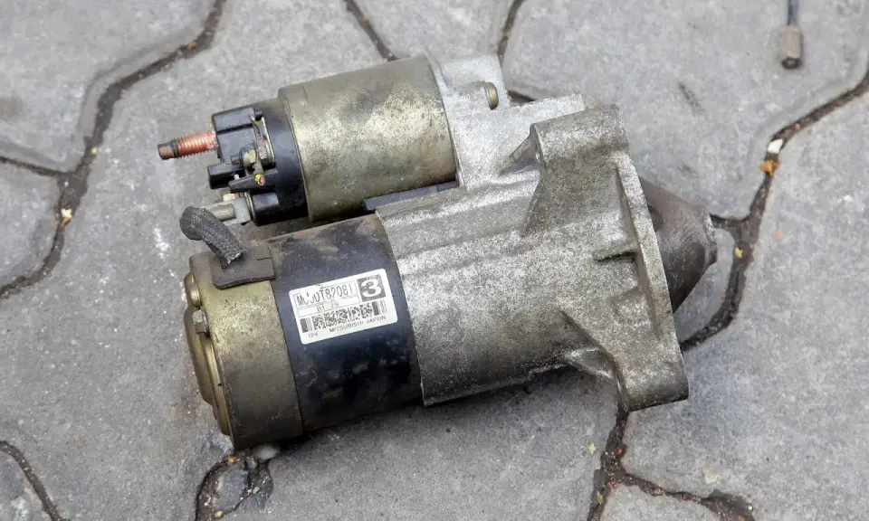 Dwa używane rozruszniki samochodowe, gotowe do wymiany. Jeden z nich ma naklejkę z numerem MC0JT82081.