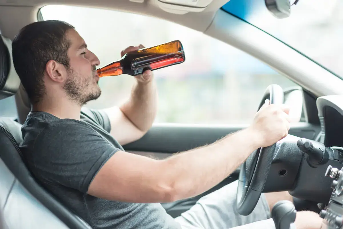Mężczyzna pije piwo za kierownicą. Powyżej 0,5 promila jaka kara grozi za jazdę pod wpływem alkoholu.