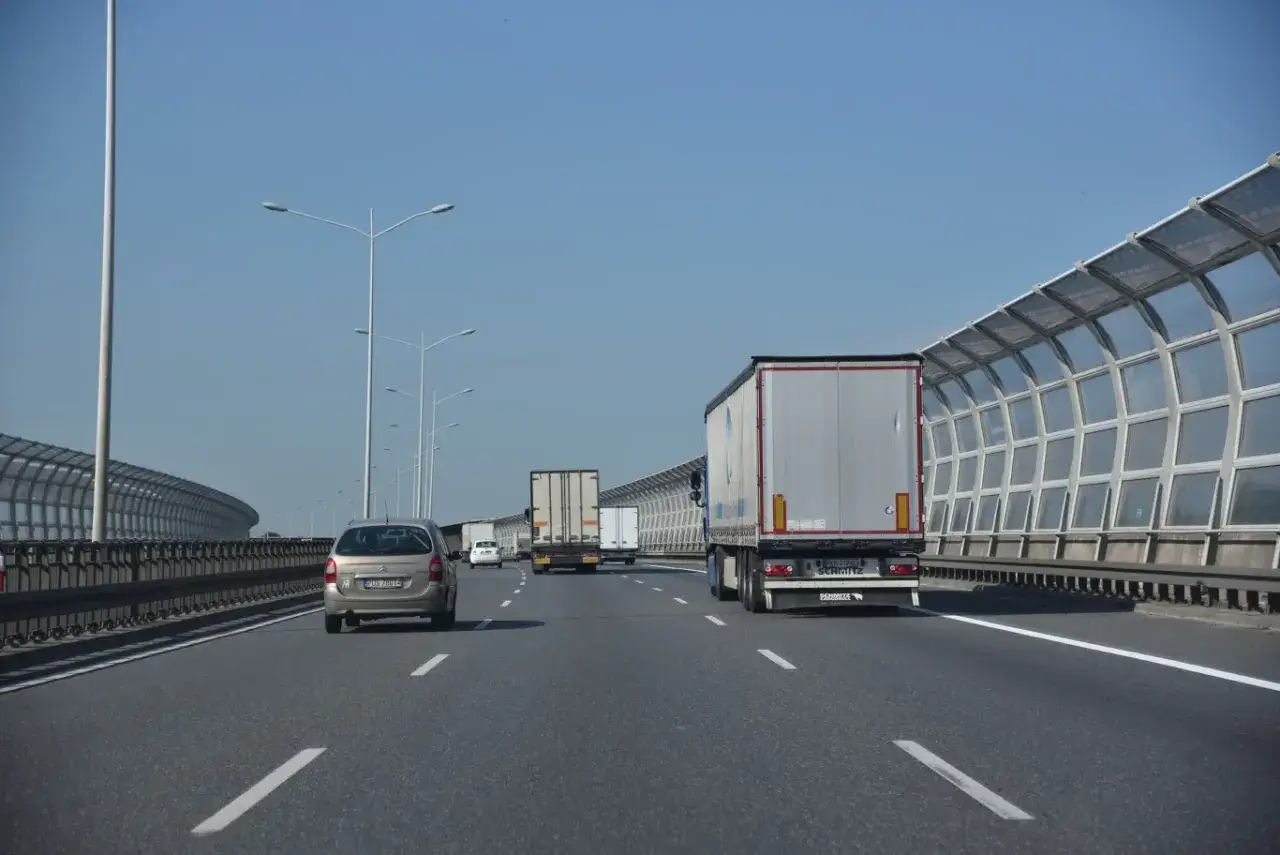 Samoch&oacute;d osobowy jedzie lewym pasem autostrady, grozi mu mandat za jazdę lewym pasem. W tle inne pojazdy i ekrany akustyczne.
