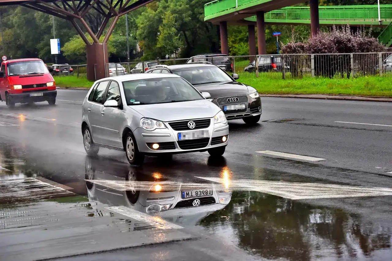 Samochody jadące po mokrej drodze, tworząc kałuże. Widać, że to aquaplaning co to za zjawisko, gdy opony tracą przyczepność na wodzie.