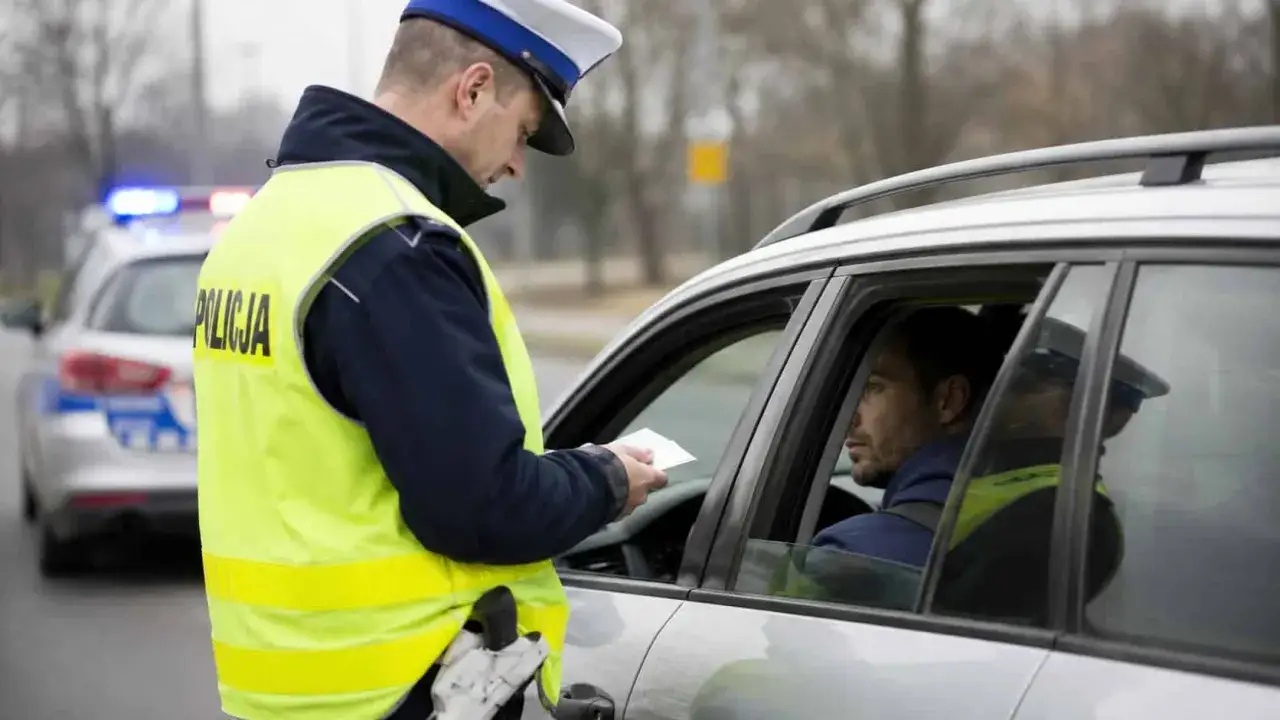 Policjant w kamizelce odblaskowej wręcza dokument kierowcy. Za takie wykroczenia można stracić prawo jazdy na 3 miesiące.