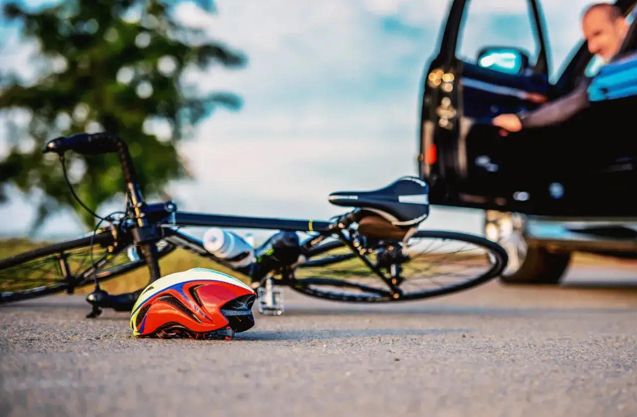 Potrącenie rowerzysty na ścieżce rowerowej. Kierowca wysiada z czarnego auta, obok leży rower i kask. Może skończyć się mandatem.