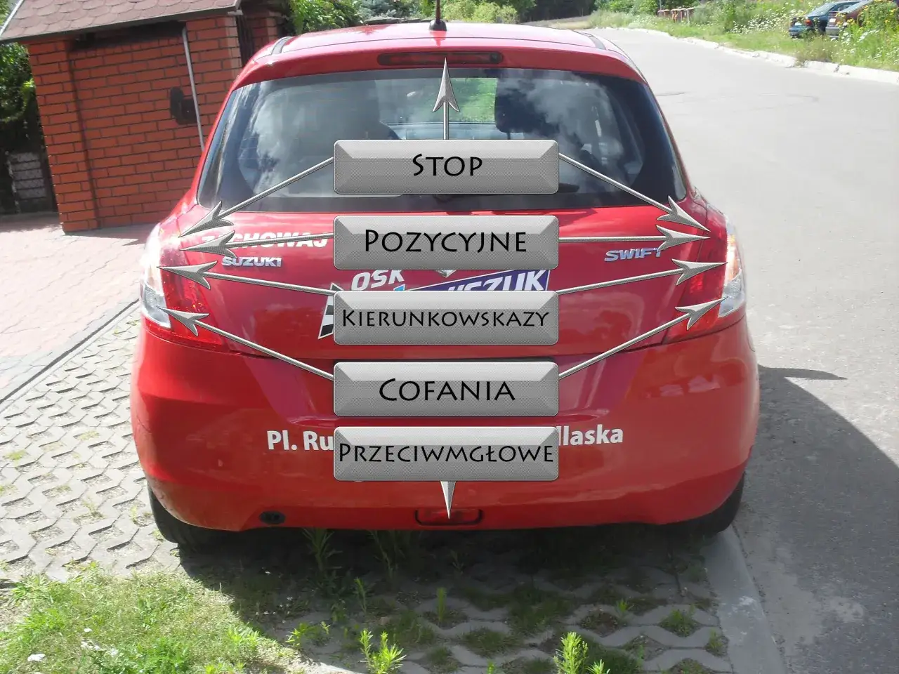 Czerwony Suzuki Swift z naklejkami informującymi o światłach w samochodzie egzamin: stop, pozycyjne, kierunkowskazy, cofania, przeciwmgłowe.