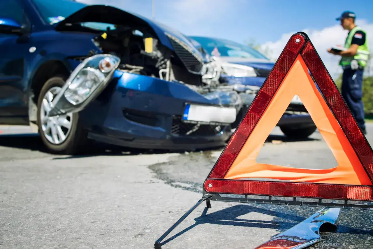Tr&oacute;jkąt ostrzegawczy przed uszkodzonymi autami. Policjant spisuje zeznania po spowodowaniu wypadku z uszczerbku na zdrowiu powyżej 7 dni.