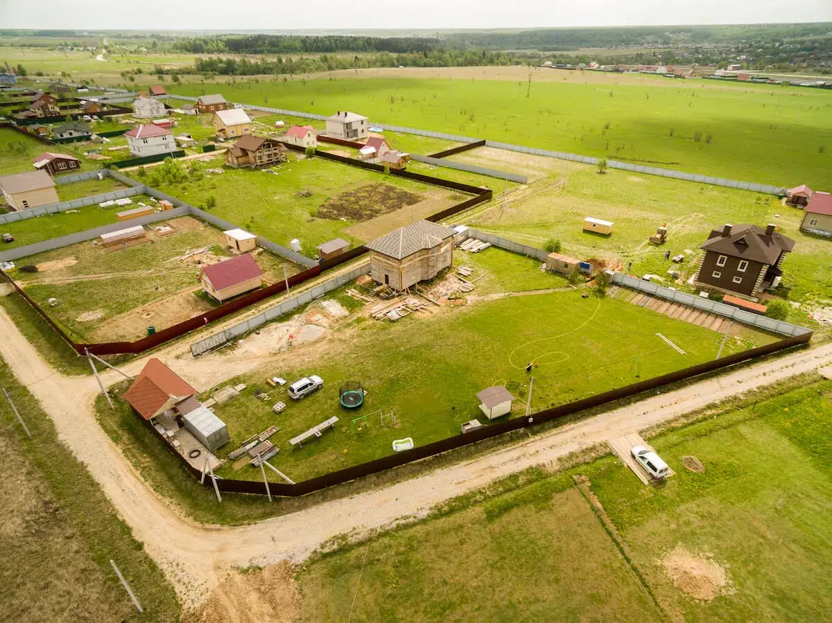 Działka z domem w budowie, problemy z dojazdem do posesji. Widać domy, ogrodzenia, samochody i plac budowy.