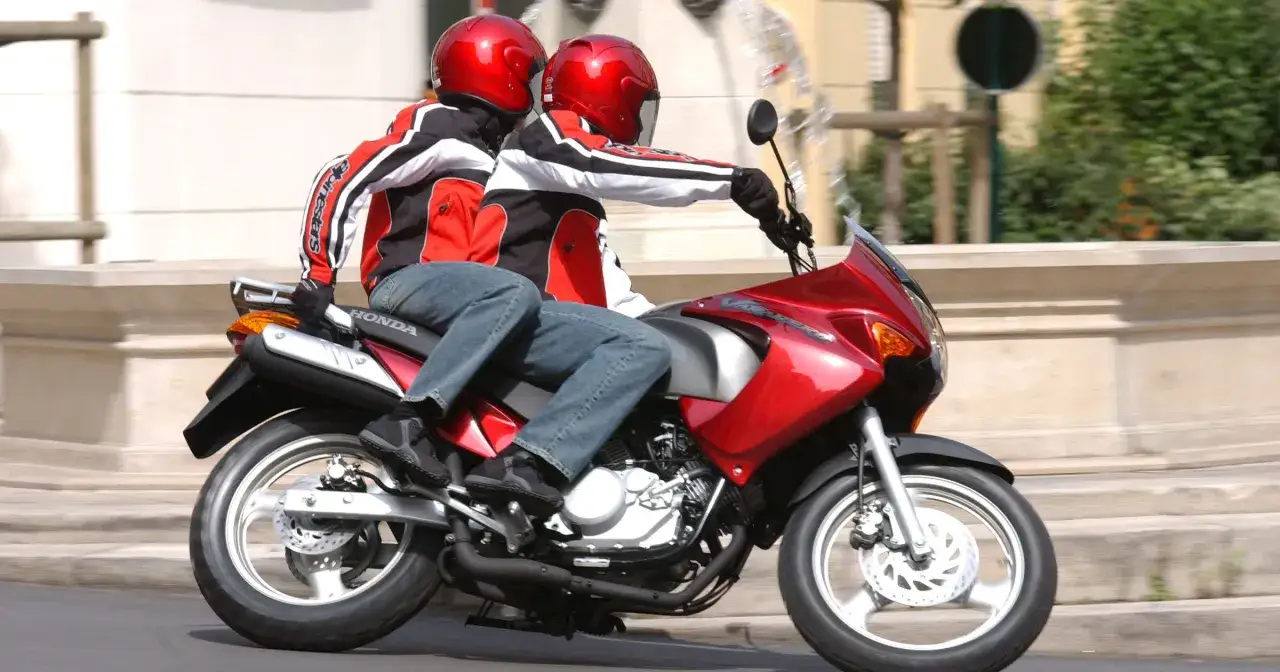 Dwie osoby w czerwonych kaskach jadą na czerwonym motocyklu Honda. Czy na motor 125 trzeba mieć prawo jazdy? Tak, do prowadzenia motocykla 125ccm potrzebne jest prawo jazdy kategorii A1.
