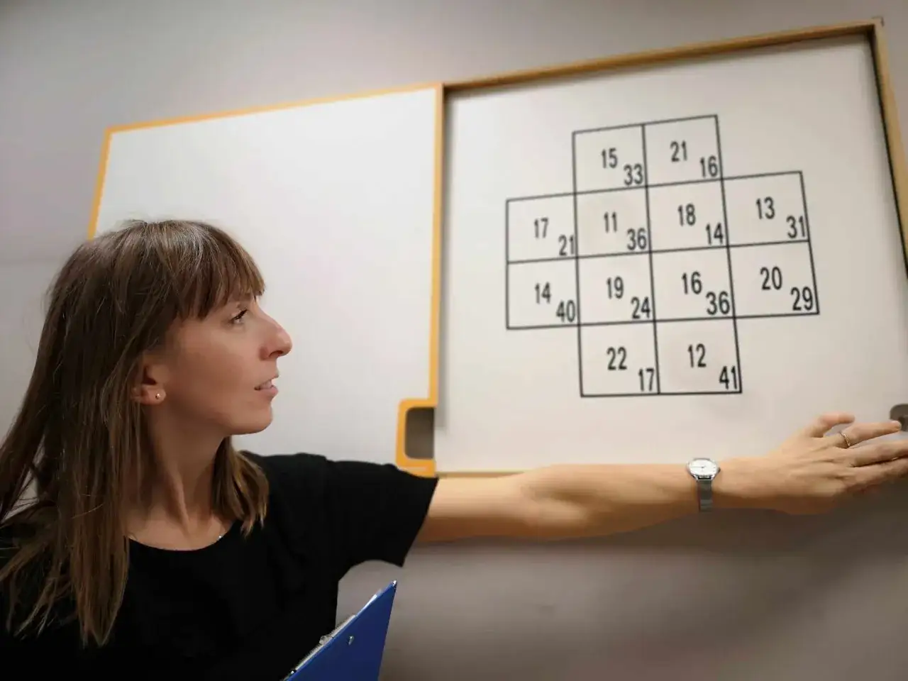 Psycholog przeprowadza test psychologiczny dla kierowców, wskazując na tablicę z liczbami.