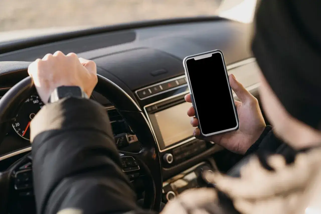 Kierowca trzyma telefon, zastanawiając się, ile punkt&oacute;w za telefon straci.