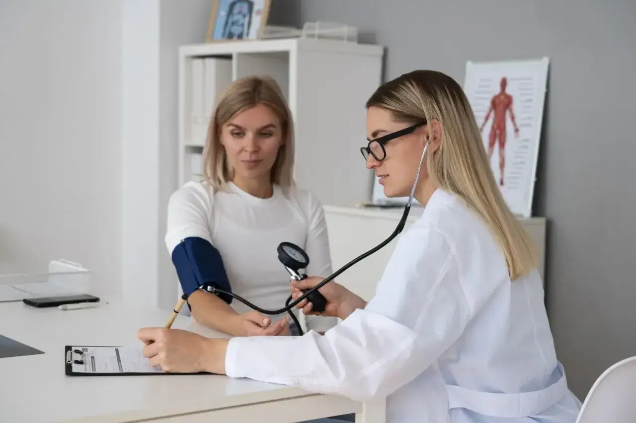 Lekarka mierzy ciśnienie kobiecie, co jest częścią tego, jak wygląda badanie na prawo jazdy. Lekarka notuje wyniki.