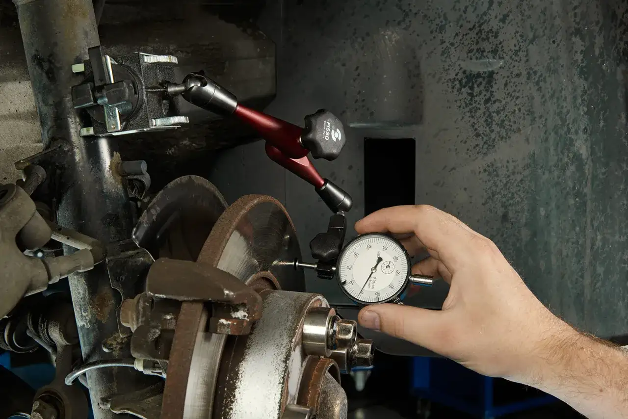 Mechanik mierzy bicie tarczy hamulcowej, aby wyeliminować drgania kierownicy przy hamowaniu.